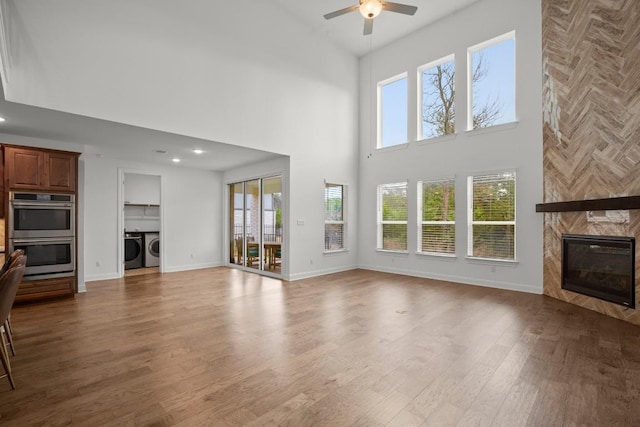 unfurnished living room with a large fireplace, hardwood / wood-style floors, a towering ceiling, ceiling fan, and washing machine and dryer