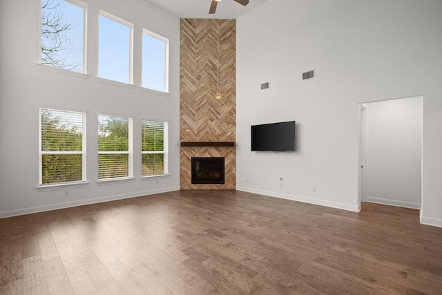 unfurnished living room with ceiling fan, dark hardwood / wood-style flooring, a tiled fireplace, and a high ceiling