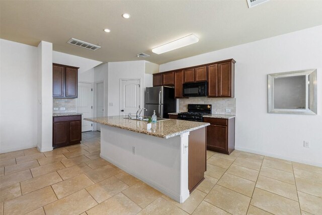 kitchen with sink, a kitchen island with sink, light stone counters, tasteful backsplash, and black appliances