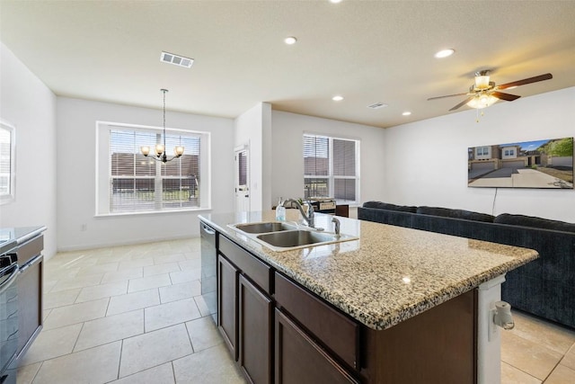 kitchen with sink, hanging light fixtures, dark brown cabinets, light stone counters, and an island with sink