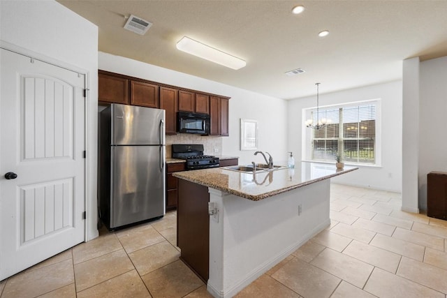 kitchen with sink, hanging light fixtures, light stone counters, black appliances, and a center island with sink