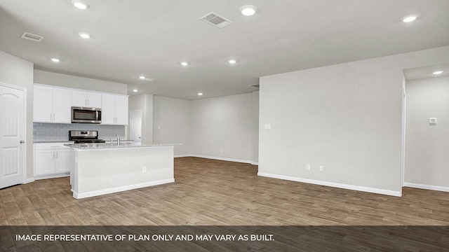 kitchen with appliances with stainless steel finishes, hardwood / wood-style floors, a center island with sink, and white cabinets