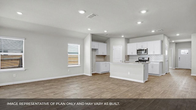 kitchen with a kitchen island with sink, backsplash, white cabinetry, stainless steel appliances, and light wood-type flooring