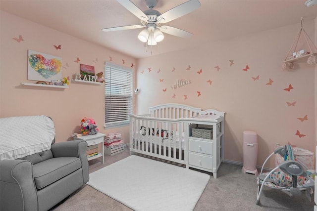 bedroom featuring a nursery area, ceiling fan, and light carpet