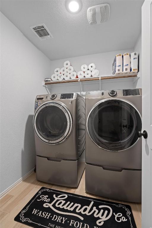 clothes washing area featuring separate washer and dryer, wood-type flooring, and a textured ceiling