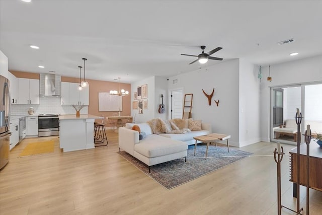 living area with light wood finished floors, recessed lighting, visible vents, baseboards, and ceiling fan with notable chandelier