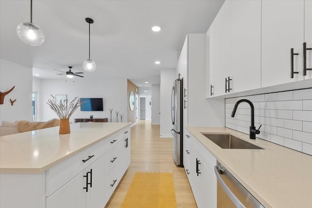 kitchen featuring pendant lighting, white cabinetry, sink, stainless steel appliances, and light hardwood / wood-style flooring