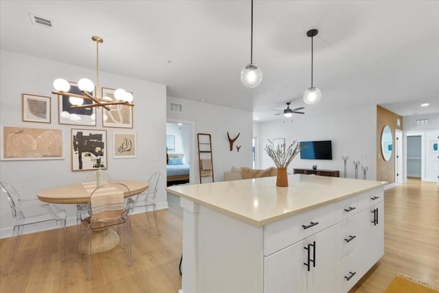 kitchen with pendant lighting, a center island, light hardwood / wood-style floors, white cabinets, and ceiling fan with notable chandelier