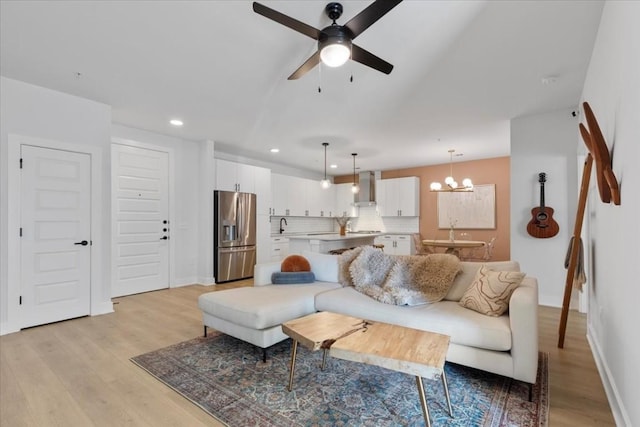 living room featuring ceiling fan with notable chandelier and light wood-type flooring