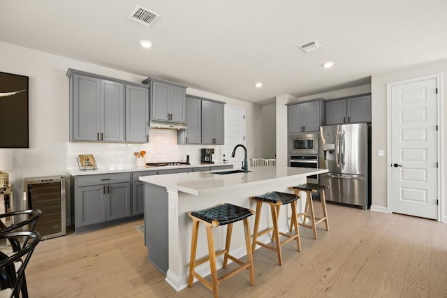 kitchen featuring sink, gray cabinets, appliances with stainless steel finishes, an island with sink, and a kitchen bar