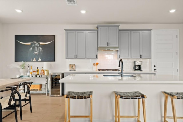 kitchen featuring sink, beverage cooler, a kitchen breakfast bar, and light hardwood / wood-style flooring