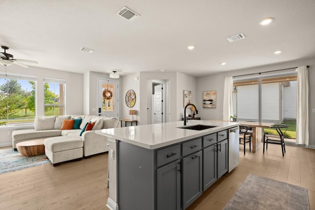 kitchen featuring sink, light hardwood / wood-style flooring, gray cabinets, dishwasher, and a kitchen island with sink