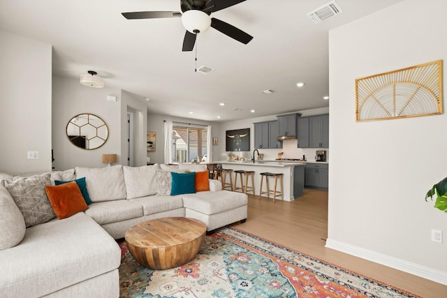 living room featuring ceiling fan, sink, and light hardwood / wood-style floors