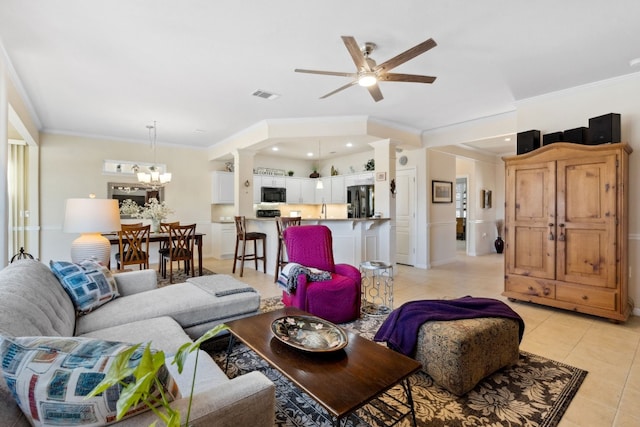 tiled living room featuring ceiling fan with notable chandelier, ornamental molding, and decorative columns