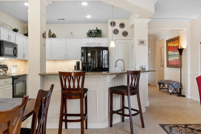 kitchen featuring ornate columns, white cabinetry, hanging light fixtures, light stone counters, and black appliances