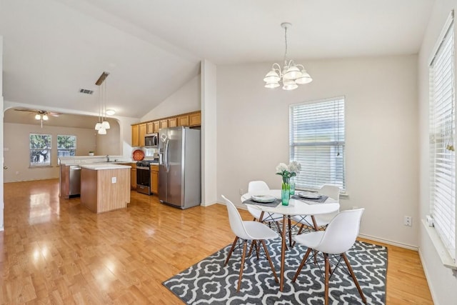 dining space featuring sink, ceiling fan with notable chandelier, high vaulted ceiling, and light wood-type flooring