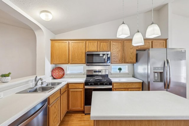 kitchen featuring decorative light fixtures, lofted ceiling, sink, stainless steel appliances, and light hardwood / wood-style flooring