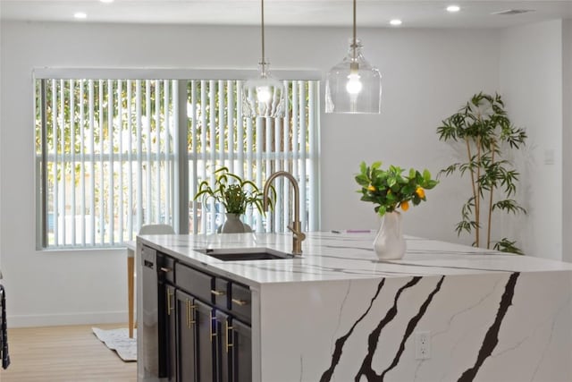 kitchen featuring sink, light hardwood / wood-style flooring, light stone countertops, a center island with sink, and decorative light fixtures