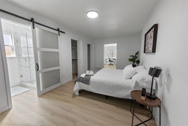 bedroom with ensuite bathroom, a barn door, and light hardwood / wood-style flooring