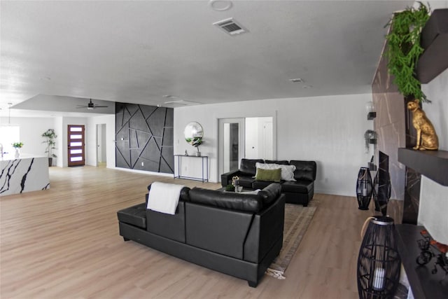 living room with a fireplace, ceiling fan, and light hardwood / wood-style flooring