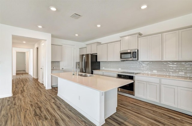 kitchen with an island with sink, wood-type flooring, sink, decorative backsplash, and stainless steel appliances