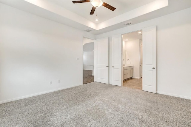 unfurnished bedroom with light carpet, connected bathroom, a raised ceiling, and ceiling fan