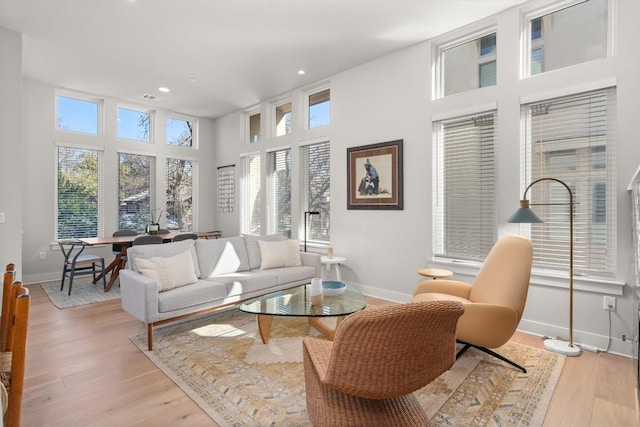 living room with a healthy amount of sunlight, light wood-type flooring, and a towering ceiling