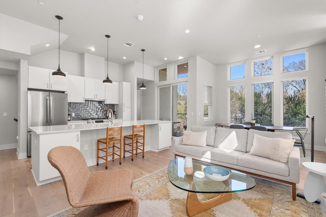 living room featuring a high ceiling, sink, and light wood-type flooring