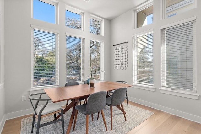 dining area featuring a towering ceiling, plenty of natural light, and light hardwood / wood-style floors