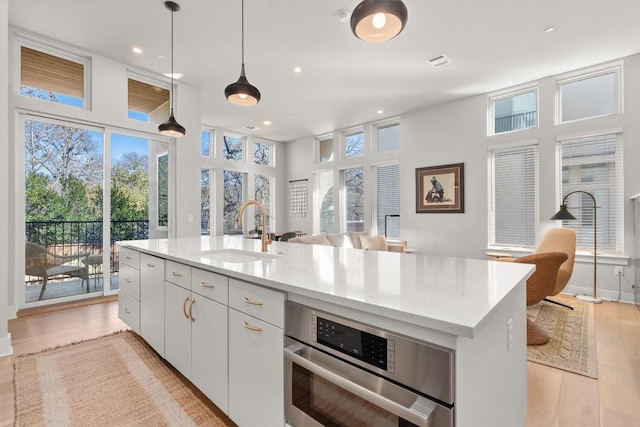 kitchen featuring sink, white cabinetry, hanging light fixtures, a center island with sink, and stainless steel oven