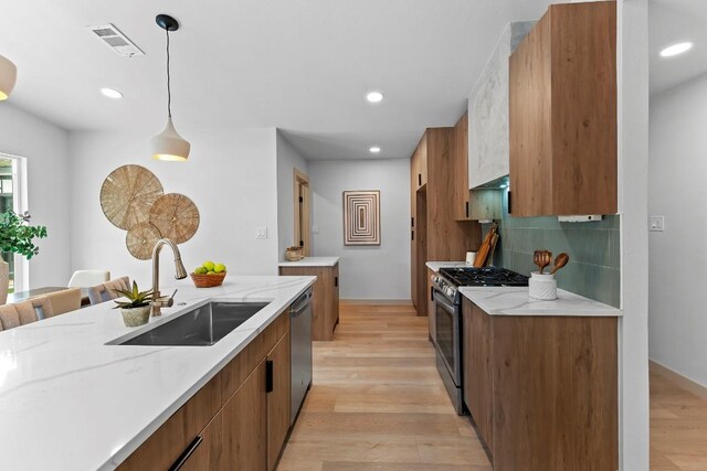 kitchen featuring sink, appliances with stainless steel finishes, hanging light fixtures, backsplash, and light hardwood / wood-style floors