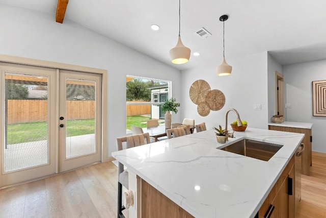 kitchen with a kitchen island with sink, sink, vaulted ceiling with beams, and hanging light fixtures