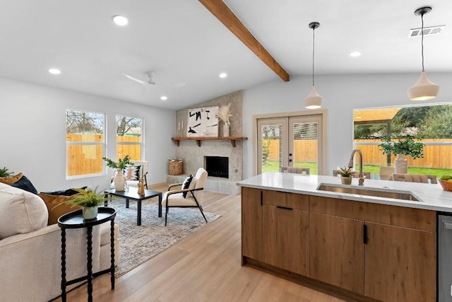 kitchen with sink, vaulted ceiling with beams, a large fireplace, decorative light fixtures, and light wood-type flooring