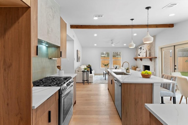 kitchen with appliances with stainless steel finishes, decorative light fixtures, sink, light hardwood / wood-style floors, and beam ceiling