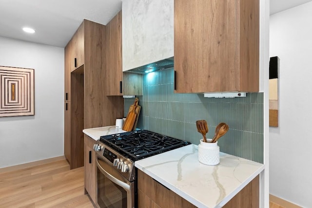 kitchen with tasteful backsplash, stainless steel range with gas cooktop, light stone counters, and light hardwood / wood-style flooring