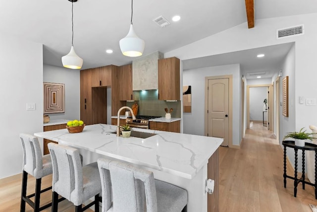 kitchen featuring pendant lighting, sink, a kitchen island with sink, vaulted ceiling with beams, and light wood-type flooring