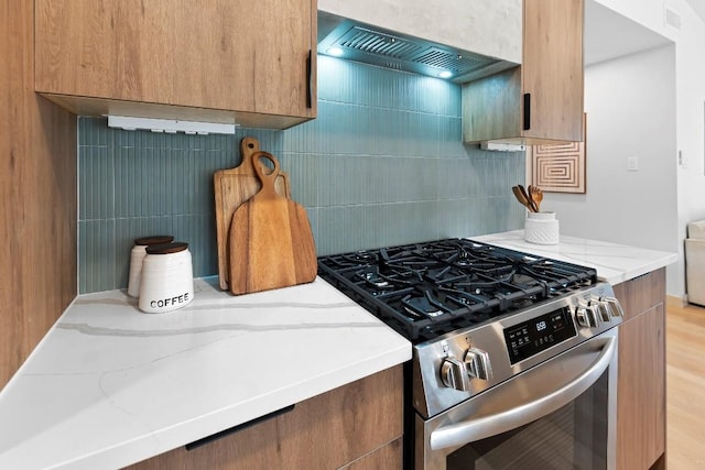 kitchen featuring premium range hood, light wood-type flooring, stainless steel range with gas cooktop, light stone countertops, and backsplash