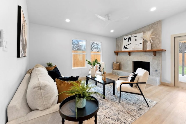 living room with ceiling fan, a large fireplace, lofted ceiling, and light hardwood / wood-style flooring