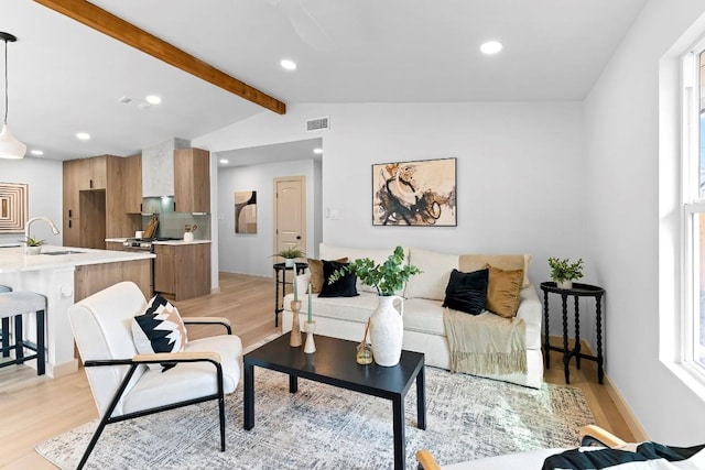 living room with vaulted ceiling with beams, sink, and light wood-type flooring