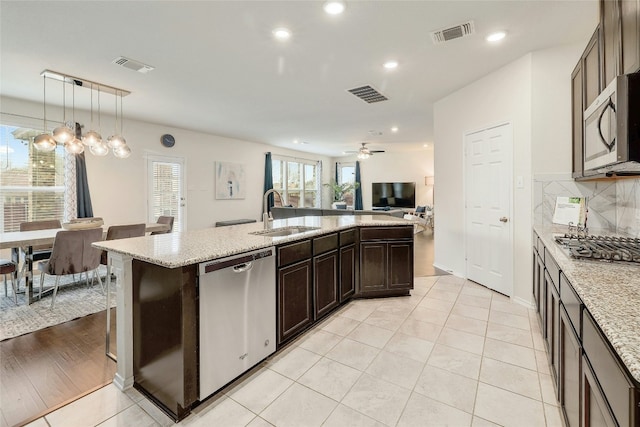 kitchen featuring appliances with stainless steel finishes, decorative light fixtures, sink, dark brown cabinetry, and light stone countertops