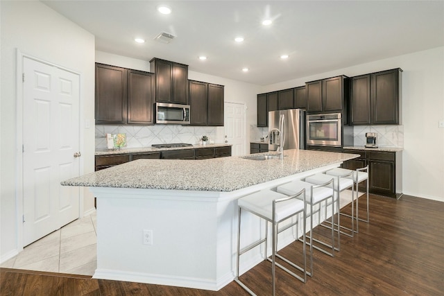 kitchen with an island with sink, sink, a breakfast bar area, dark brown cabinetry, and stainless steel appliances