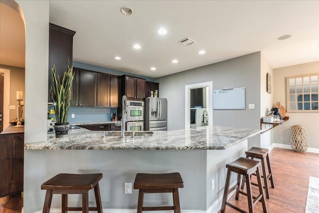 kitchen featuring kitchen peninsula, light hardwood / wood-style floors, dark brown cabinetry, stainless steel appliances, and light stone countertops