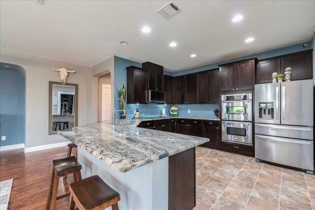 kitchen featuring sink, a breakfast bar, appliances with stainless steel finishes, dark brown cabinetry, and light stone counters