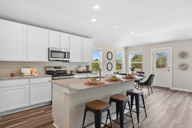 kitchen with appliances with stainless steel finishes, white cabinetry, sink, backsplash, and a kitchen island with sink