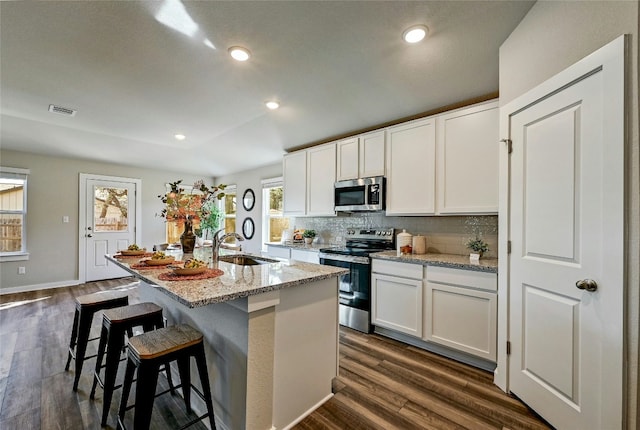 kitchen featuring an island with sink, white cabinetry, light stone countertops, sink, and appliances with stainless steel finishes