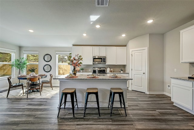 kitchen with stainless steel appliances, light stone countertops, a kitchen island with sink, white cabinetry, and a kitchen bar