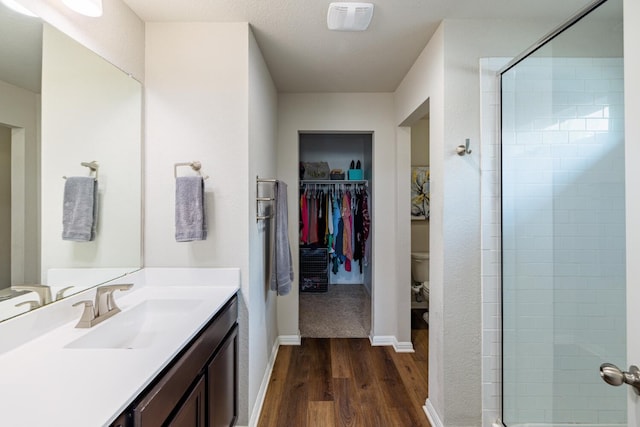 bathroom with hardwood / wood-style flooring, vanity, walk in shower, and toilet