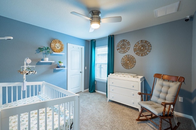 bedroom featuring a nursery area, ceiling fan, and light carpet