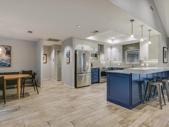 kitchen with appliances with stainless steel finishes, pendant lighting, blue cabinets, white cabinetry, and kitchen peninsula