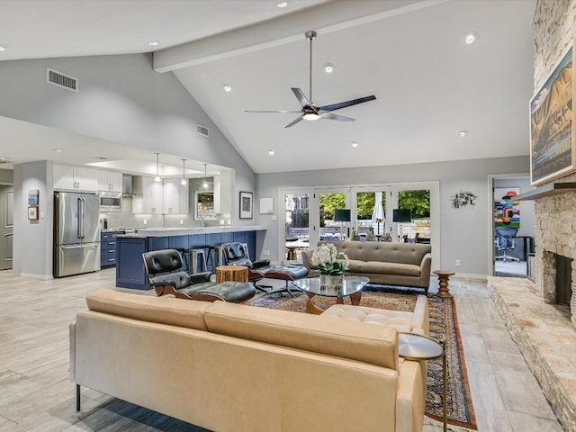 living room with beamed ceiling, ceiling fan, a stone fireplace, and high vaulted ceiling